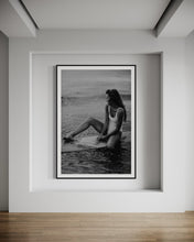 Load image into Gallery viewer, The artwork 'Riding Tide' displayed elegantly in a modern room, featuring a woman in a white swimsuit on a surfboard, framed to complement contemporary decor.