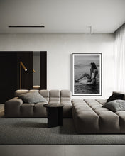 Load image into Gallery viewer, A modern living room with minimalist decor featuring the framed photography 'Riding Tide', highlighting a woman sitting on a surfboard, bringing a touch of coastal elegance.