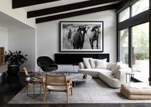 Load image into Gallery viewer, A modern living room showcasing framed Western Art featuring a herd of horses in a black and white photograph. The artwork is prominently displayed on the wall, complementing the contemporary furnishings and adding an artistic touch to the stylish interior.